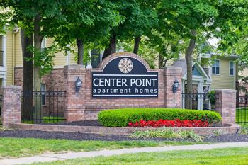 A sign for Center Point Apartment Homes is surrounded by a flower bed and trees.